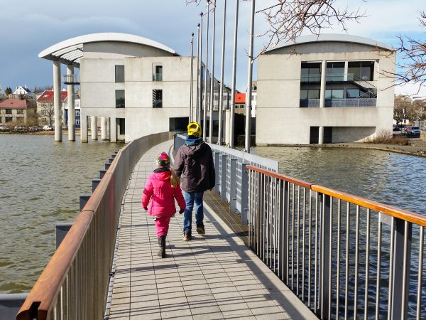 Kinder laufen über eine Brücke des Tjörnin Stadtteiches zum Rathaus