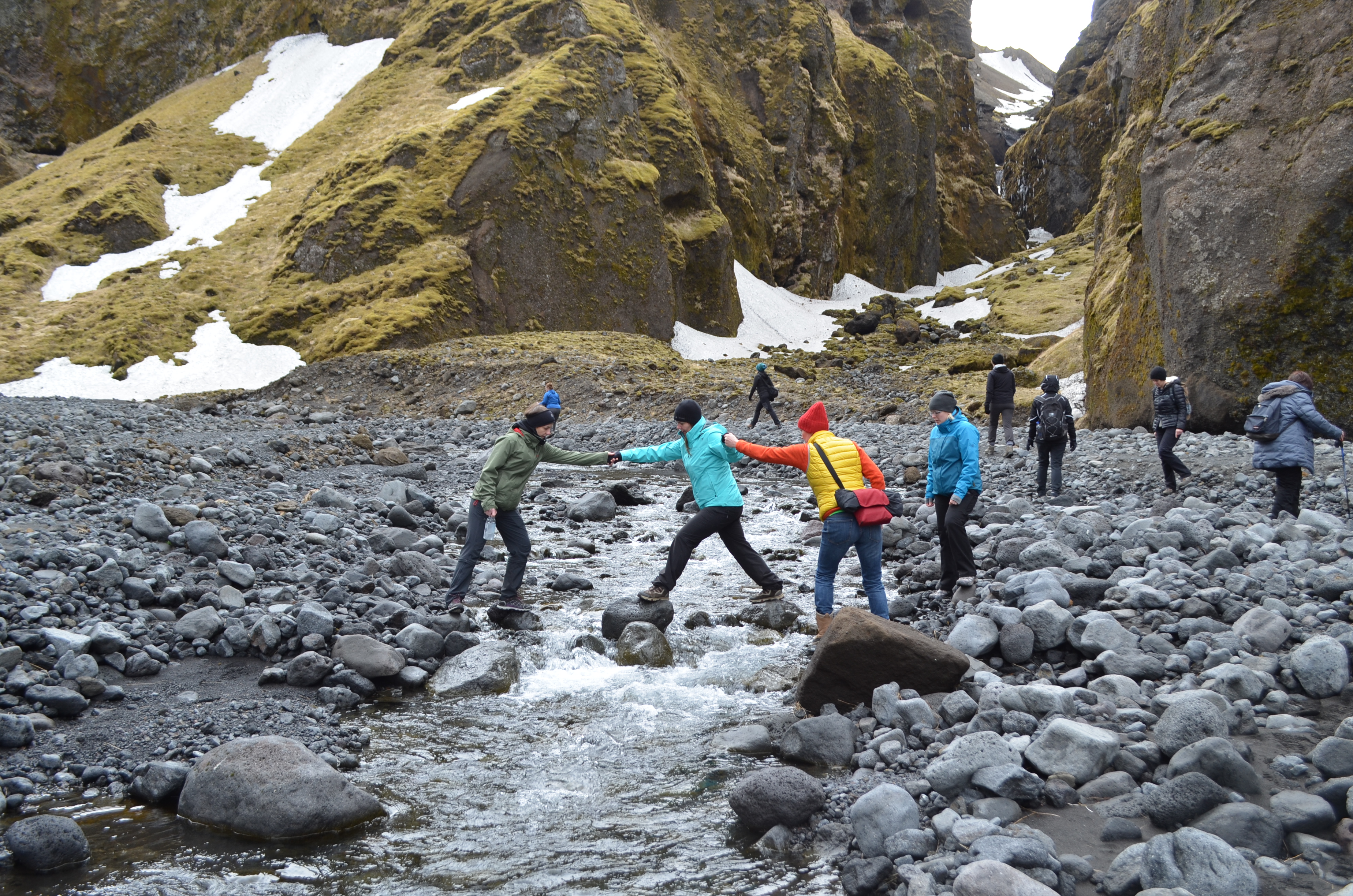 Mitglieder des Teams von Katla Travel helfen sich gegenseitig über einen Bach in Island