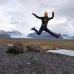 Wanderin springt vor Freude vor einem Gletscher