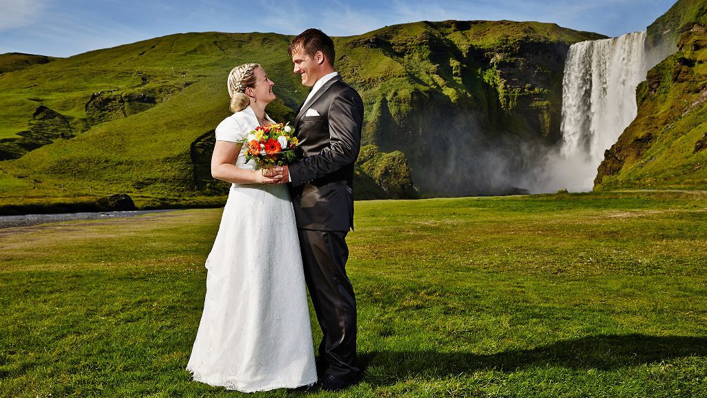 Hochzeitspaar auf grüner Wiese vor einem Wasserfall in Island