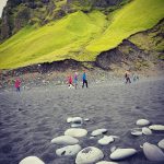 Wanderer am Strand bei Südisland, Moosbewachsene Felsen im Hintergrund