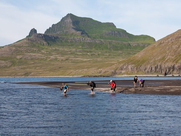 Wandergruppe in Island läuft barfuß durch einen breiten Bach